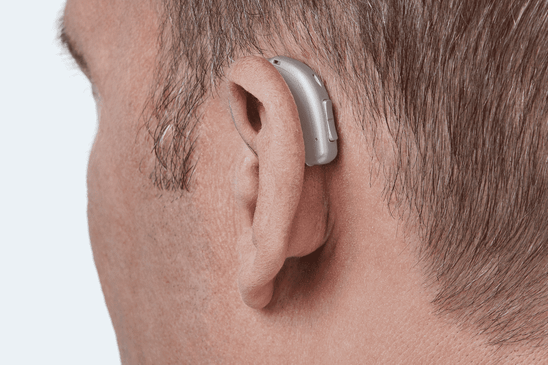 Oticon More Hörgerät, Modell miniRITE R, Farbe Hellgrau, Foto von hinten aus einem Winkel von 45° aufgenommen, Nahaufnahme am Ohr, Mann Hörgeräte mit Auzen unbegrenzter Service