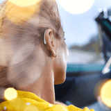 A woman driving a car wearing highly sleek white Behind the Ear Signia Styletto 3X/7X hearing aids